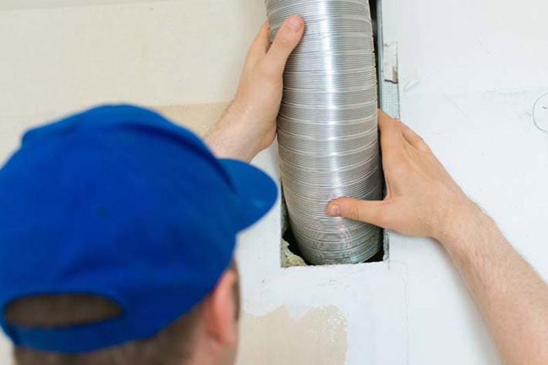 Blog Post: When Is It Time for a Split-System AC Replacement? Photo: Technician setting up ventilation system indoors.