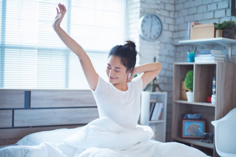 Woman sitting up in bed, stretching.